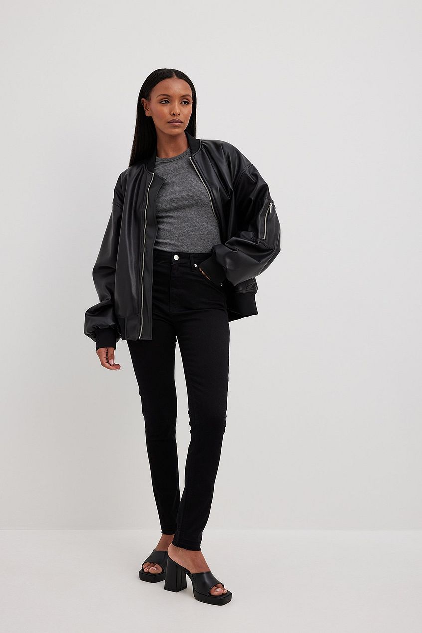 Skinny High Waist Open Hem Jeans on model, sleek black jacket, casual attire, minimalist background.