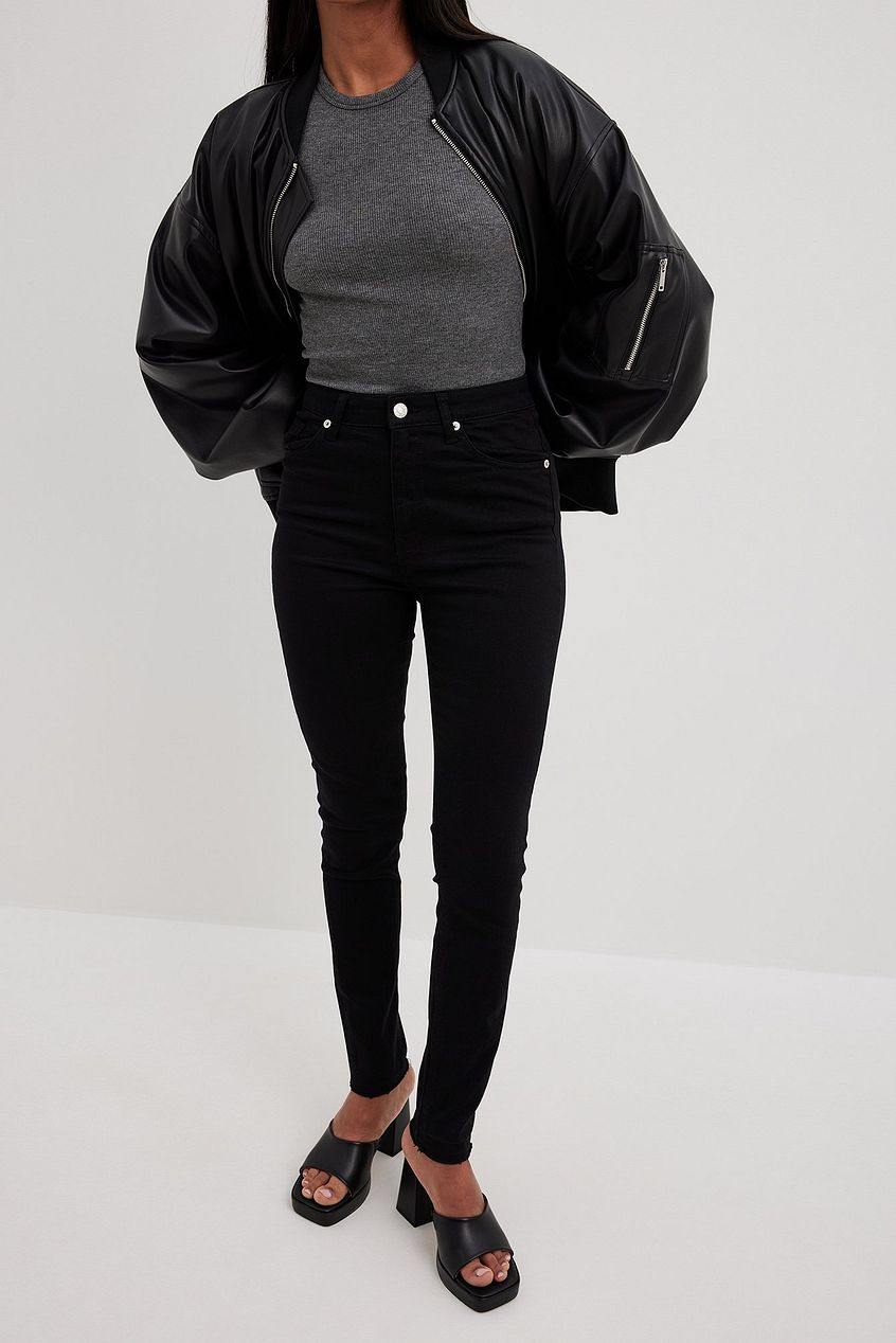 Skinny high-waist open-hem black jeans, paired with a casual gray top and a stylish black jacket, showcased on a female model.