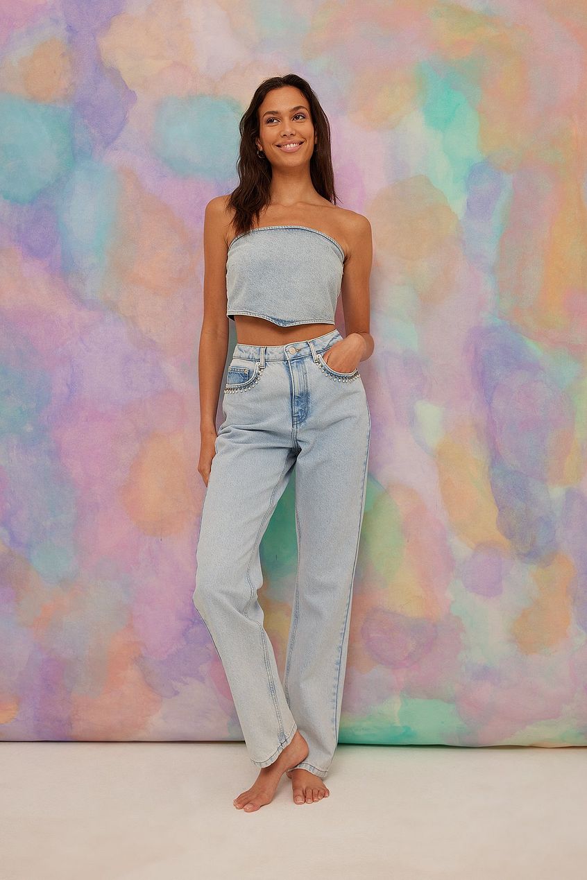 Stylish high-waisted denim jeans with rhinestone details, worn by a smiling young woman against a vibrant, pastel-colored backdrop.