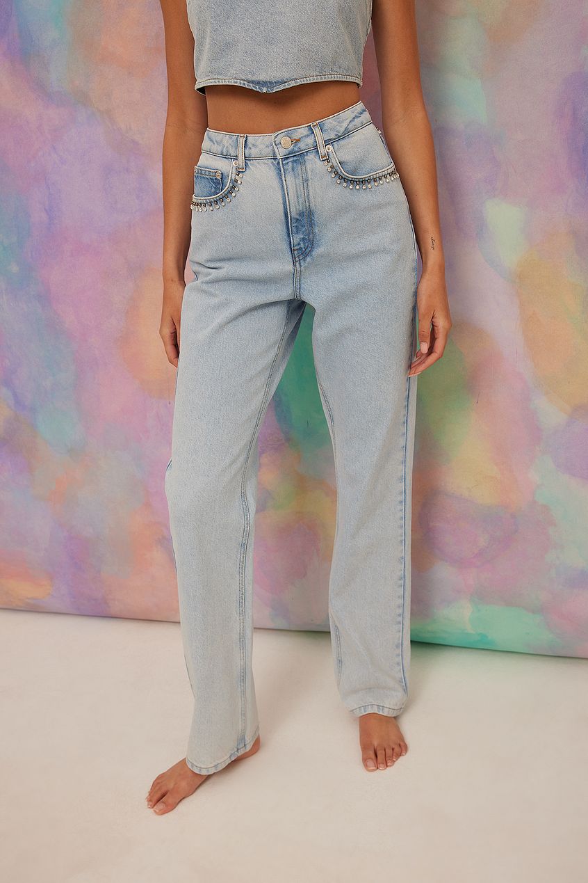 High-waisted light wash denim jeans with subtle rhinestone detailing, showcased against a vibrant pastel backdrop.