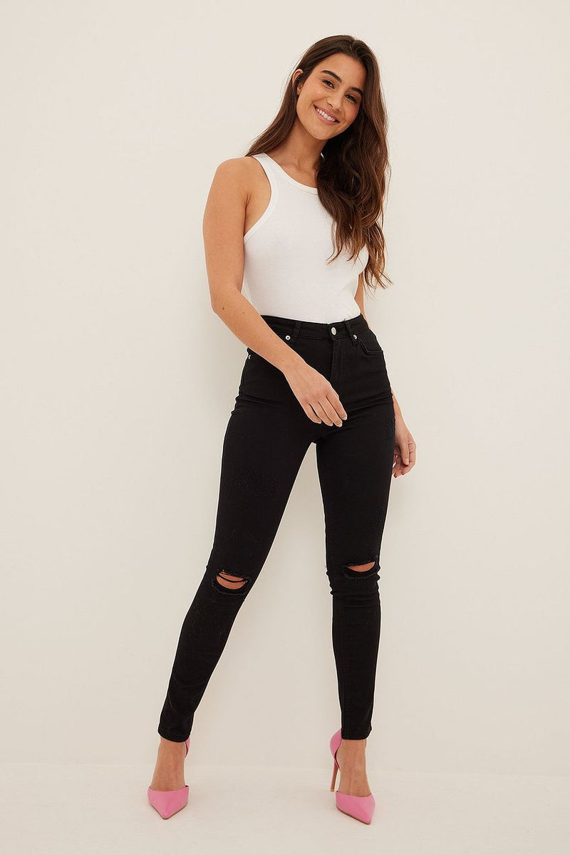 Woman wearing organic skinny high waist destroyed black jeans from Ace Cart, standing against a neutral background and smiling.