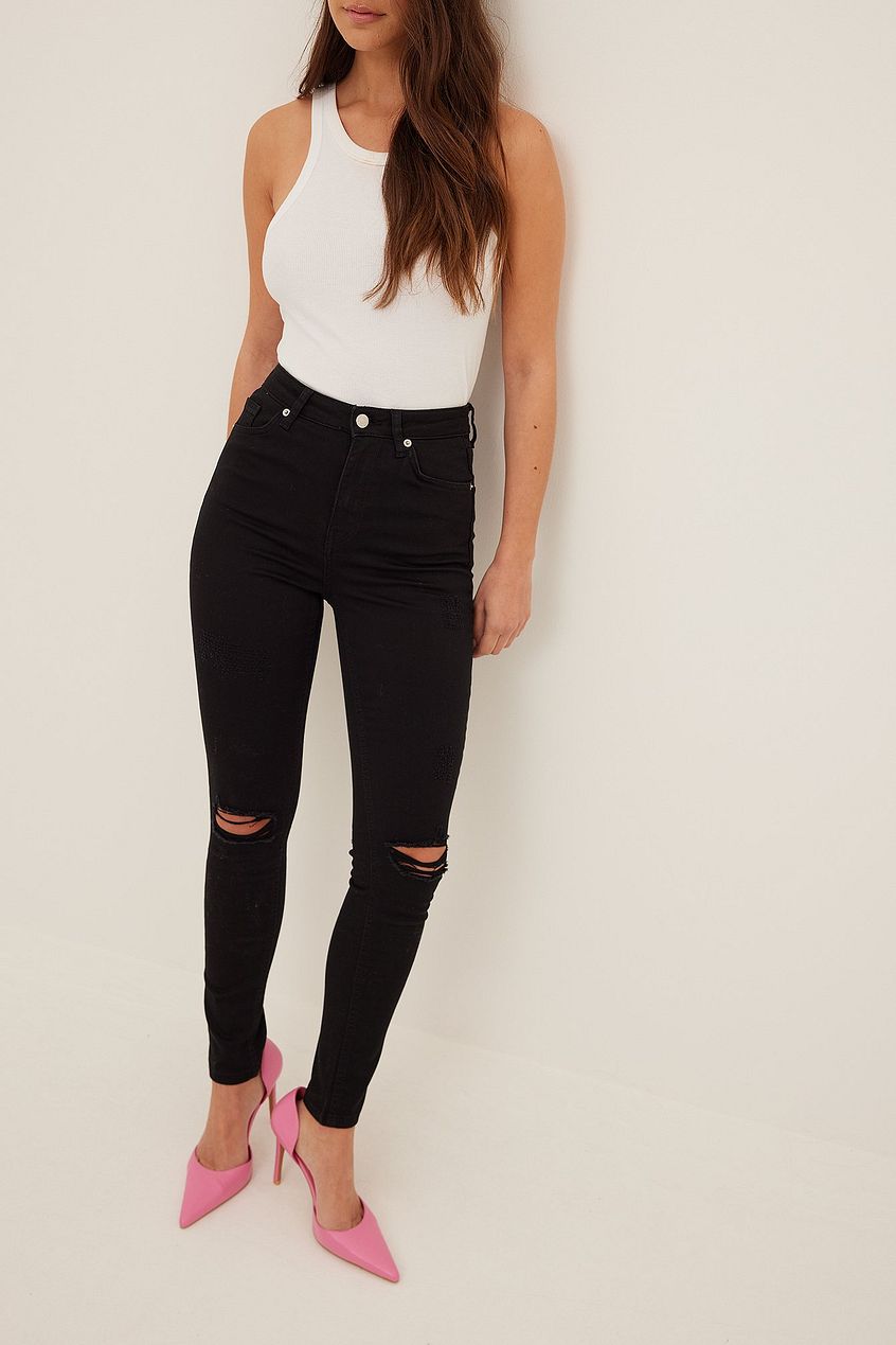 Organic skinny high waist destroyed black jeans, paired with a white tank top and pink heels, showcased against a neutral background.