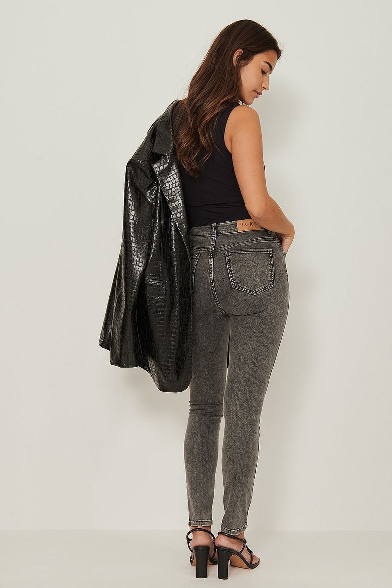 Skinny high-waist stretch jeans in grey, worn with a black tank top and leather jacket, showcasing a feminine, stylish look.