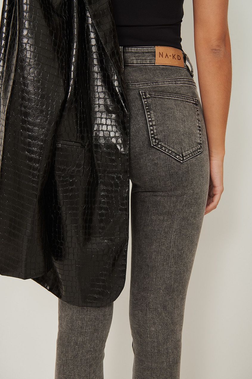 Skinny high-waist stretch jeans with a denim wash, featuring a leather-like jacket in the background.