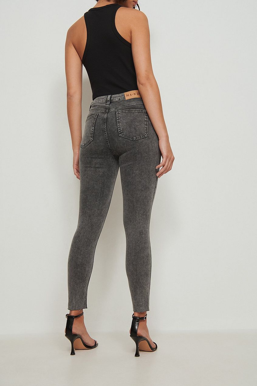 Skinny high-waist grey wash denim jeans with raw hem, worn by a female model against a white background
