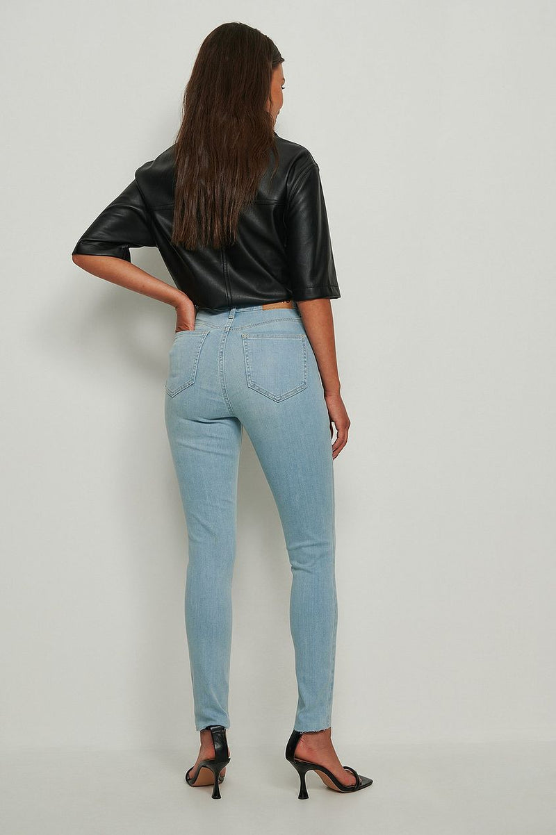 Skinny high waist raw hem light wash denim jeans with a woman wearing a black leather top and heels.