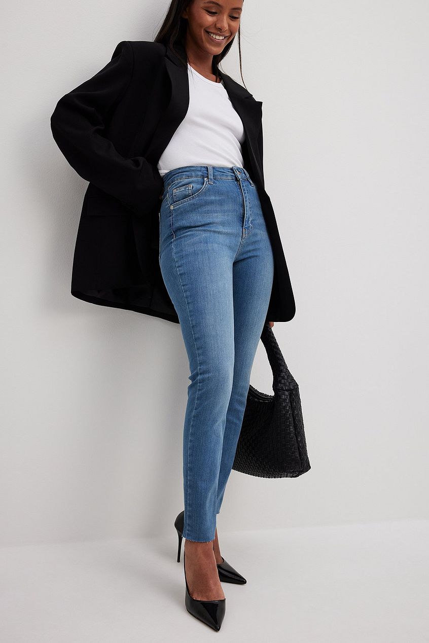Stylish high-waist denim jeans, white top, black coat, and leather handbag on young smiling woman.
