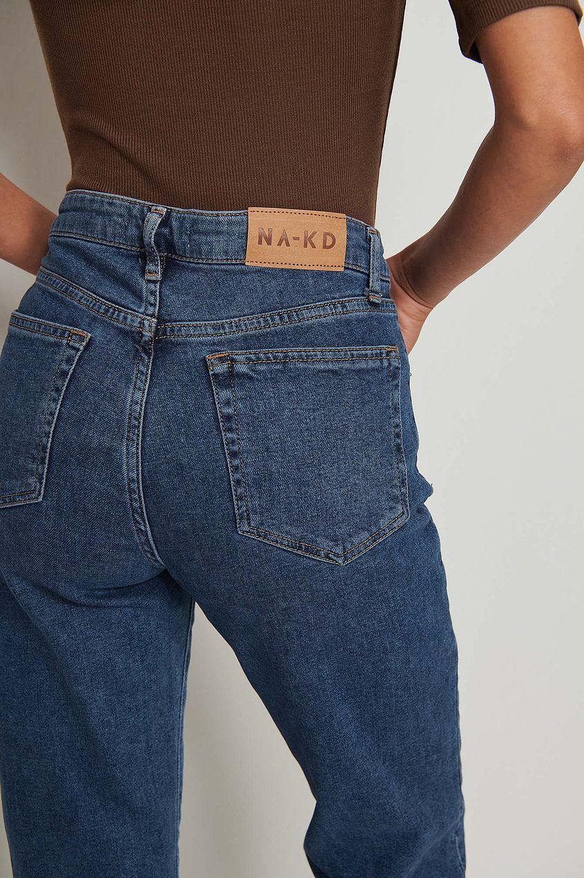 Straight mid-waist blue denim jeans with a branded leather patch on the waistband, displayed on a white background.