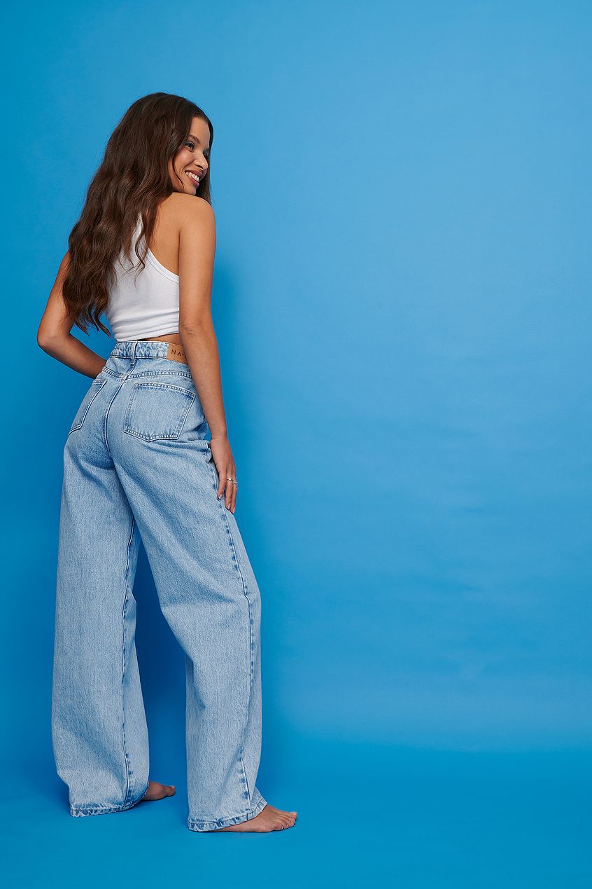 Elegant woman wearing vintage look wide leg high waist jeans posing against blue background.