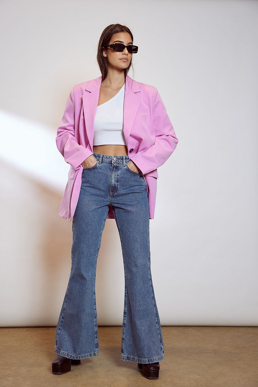 Stylish wide leg flared denim jeans with pink oversized blazer, white crop top, and sunglasses on young woman.