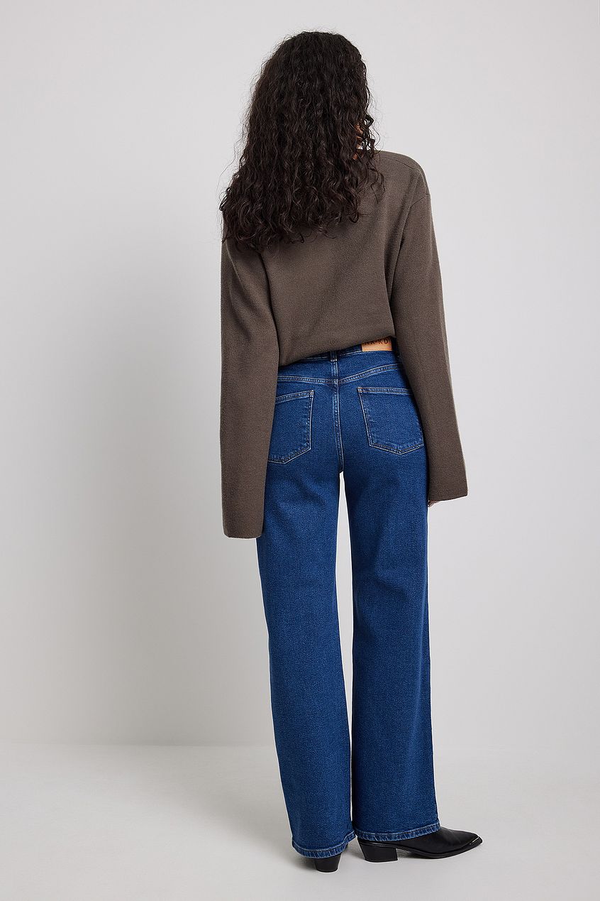 Wide leg denim jeans with high-waist design, worn by female model with curly dark hair in brown sweater on plain white background.
