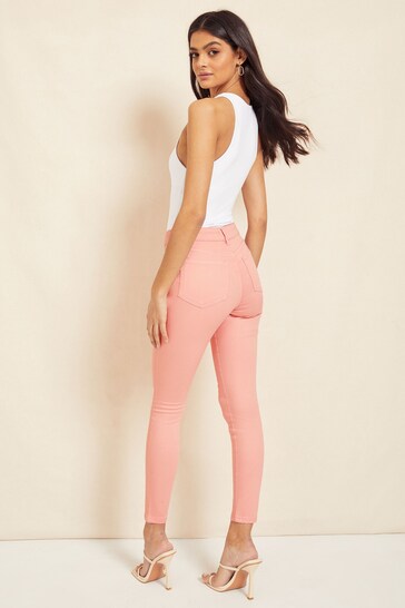 Stylish high-waisted pink jeggings with ripped knee design, worn by an attractive female model with long dark hair against a plain background.