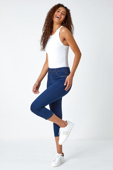 Trendy white tank top, ripped knee blue denim jeggings, and sneakers - stylish casual outfit on a smiling young woman.