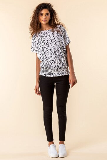 Stylish woman wearing patterned blouse and black skinny jeans, showcasing modern casual fashion.