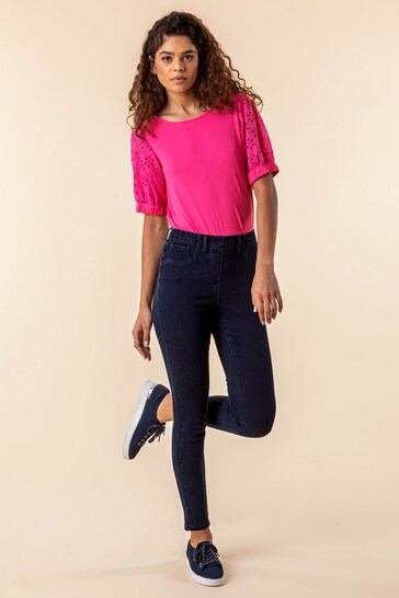 Vibrant pink blouse with lace detailing, dark blue high-waisted skinny jeans, and casual navy blue sneakers worn by a young woman with curly hair.