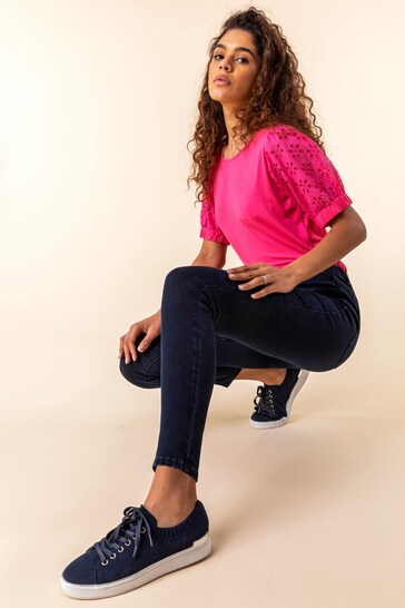 High-quality pink blouse, dark blue jeggings, and black canvas sneakers worn by a stylish young woman with curly hair posing against a plain background.