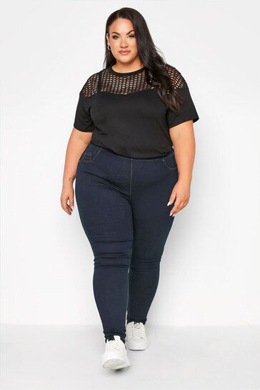 Fashionable plus-size model wearing black mesh-detail top and navy skinny jeans from Ace Cart's clothing line.
