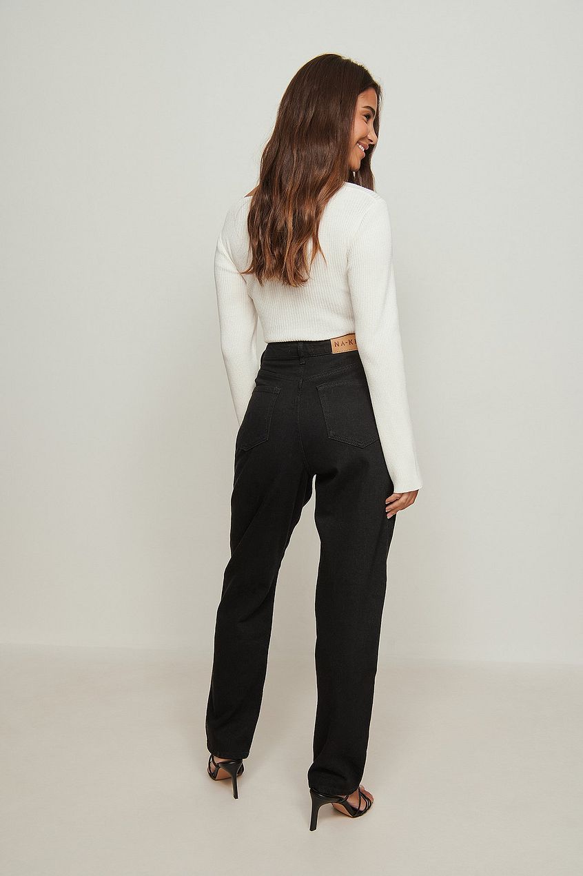 Elegant high-waist black jeans worn by a young woman with long brown hair, standing against a plain white background.