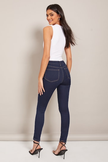 High-waisted dark blue jeggings with ripped knees, worn by a smiling young woman with long dark hair on a plain background.