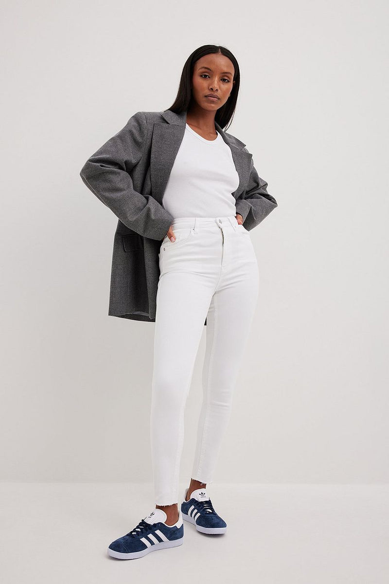 Stylish woman wearing grey coat, white top, and high-waisted white jeans, paired with navy blue sneakers