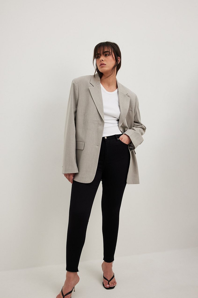 Skinny high-waist raw hem jeans, gray blazer, and minimalist sandals on a woman against a plain white background.